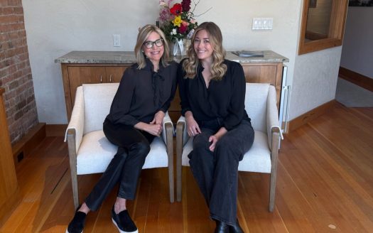two realtors sit in front in chairs by Durango, CO real estate sign