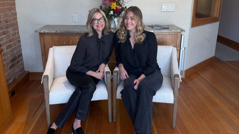 two realtors sit in front in chairs by Durango, CO real estate sign